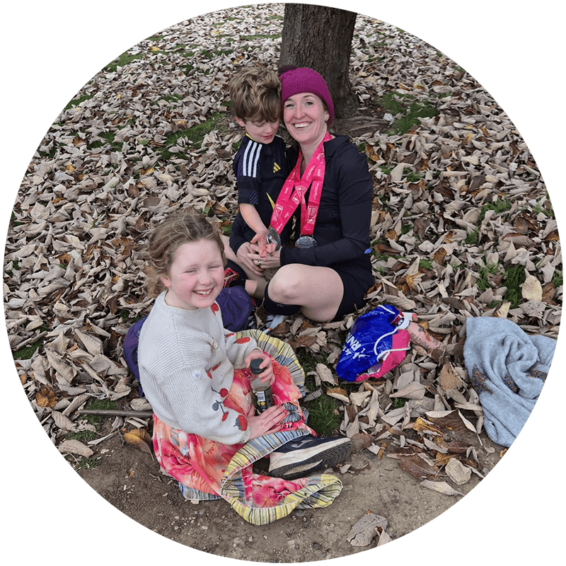 Cat, runner and online coach, relaxing after a race with her children in a park.